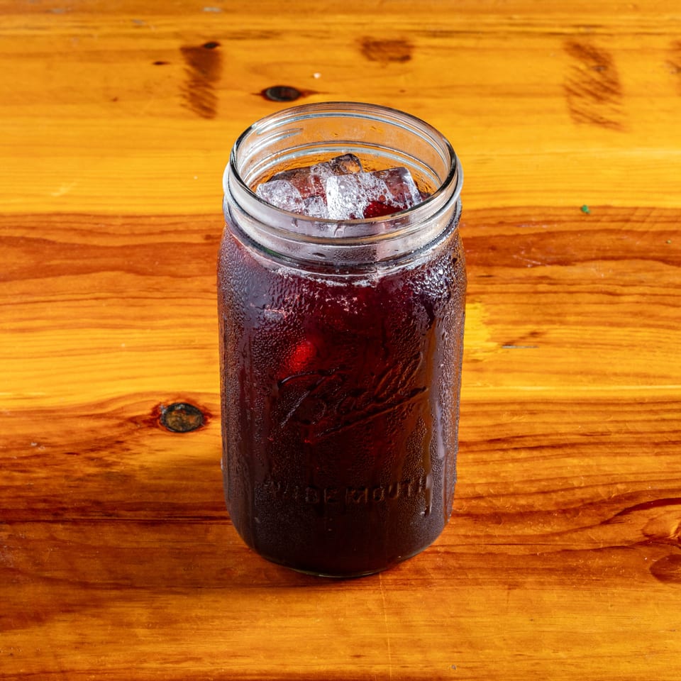 A cold, dark beverage with ice in a condensation-covered mason jar on a wooden table.