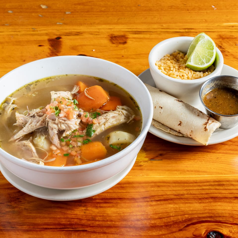 Mexican chicken soup with carrots, potatoes, pico de gallo, rice, lime, and tortillas.