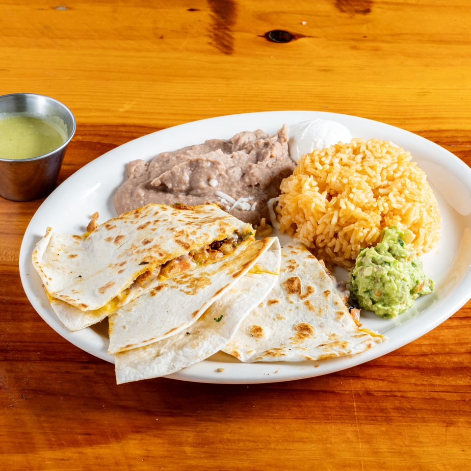 El Rey Del Grill quesadillas with rice, refried beans, guacamole, and sour cream on a white plate.