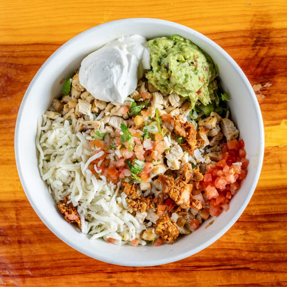 Overhead view of a Mexican burrito bowl with chicken, cheese, pico de gallo, guacamole, and sour cream.
