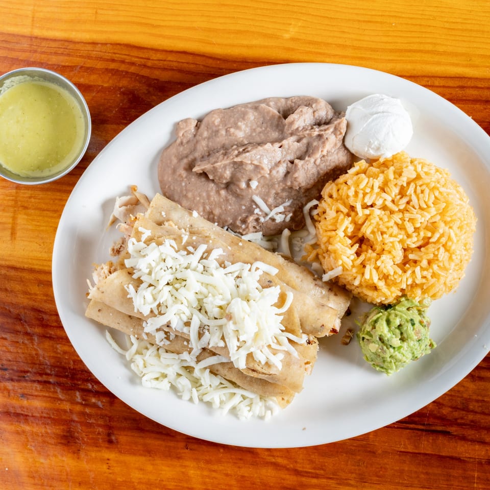 El Rey Del Grill's Mexican plate with flautas, rice, refried beans, guacamole, sour cream, and green salsa.