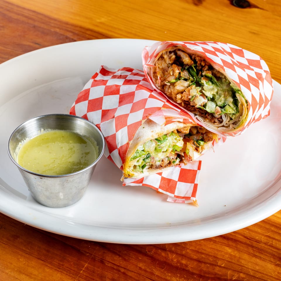 Two El Rey Del Grill burritos, cut in half, with green salsa on a white plate.